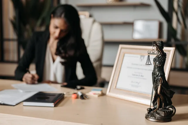 Focused woman writing at desk with Lady Justice figurine and certificate in office. How to check a children's talent agent in England