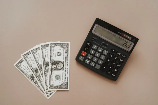 A calculator displaying '26.3' beside four one-dollar bills on a beige background. Talent agencies: VAT and illustrative cost assumptions