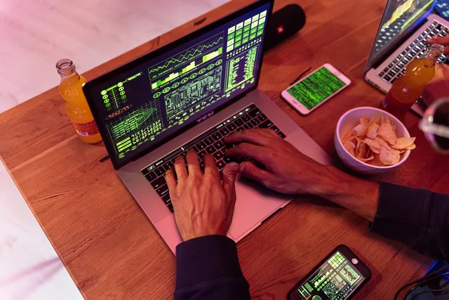 Hands typing on a laptop with coding, phone on desk, symbolizing cybersecurity. Data protection roles and transfers for talent agencies