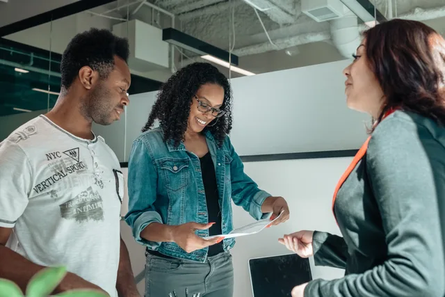 Three adults engaging in a business discussion in a bright, modern office setting. Talent agencies foundations in England: how to build a creator agency