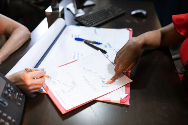 Two people discussing graphs and data on a desk, pointing and writing notes. Why talent agencies review methodology matters before you shortlist